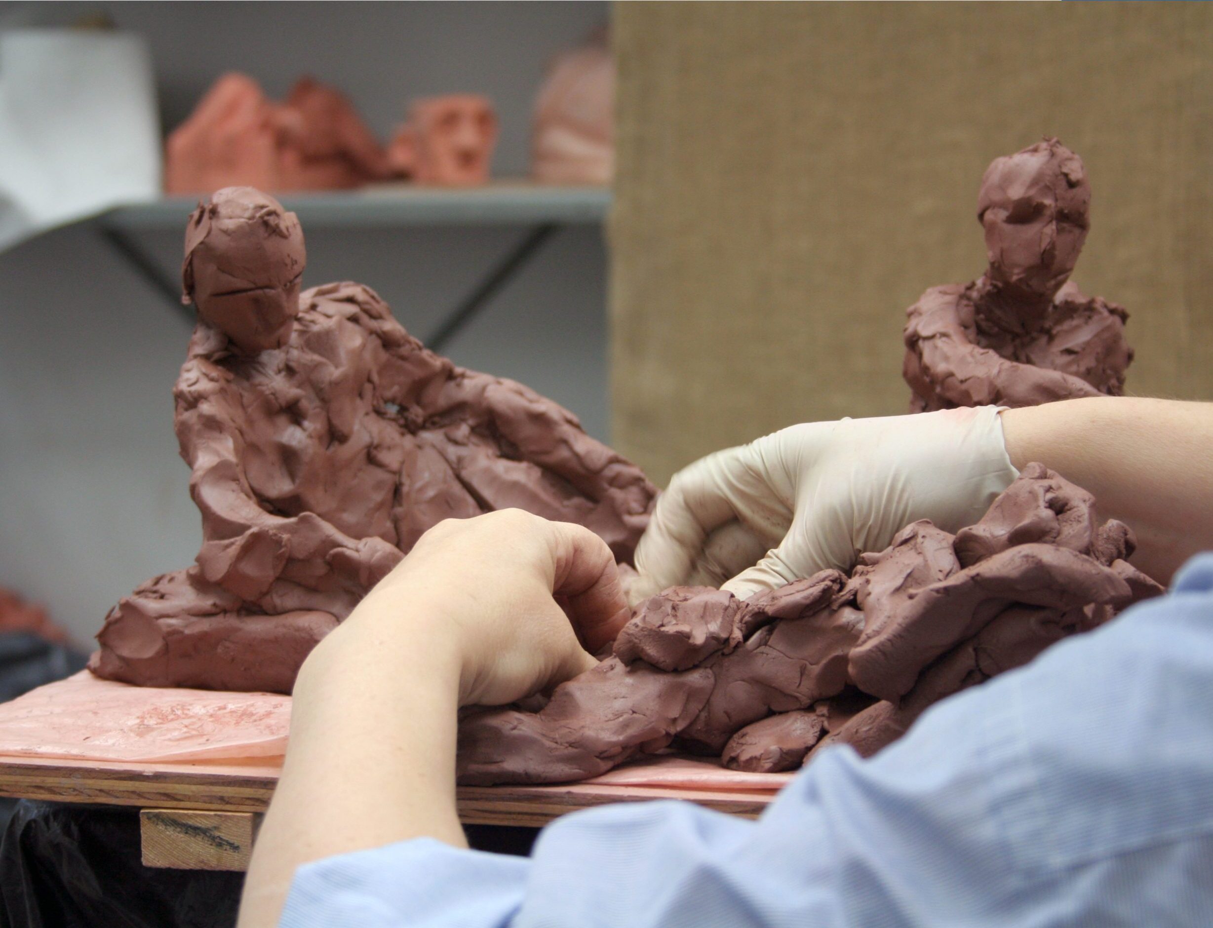 Hands sculpting a figure in clay