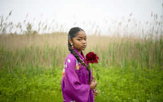 Hidemi Takagi, Mikua from the "IDENTITIES" series, 2022, Digital C Print on the textile. Shows a colored girl wearing purple. She has large, colorful earrings and is holding a red flower.