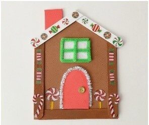 A mixed media 2-D gingerbread house. The sides are made up of brown popsicle sticks and the roof is white popsicle sticks. The wall, chimney, door, and window are made up of felt and pipe cleaners. Everything is decorated with candy cane and mint images.