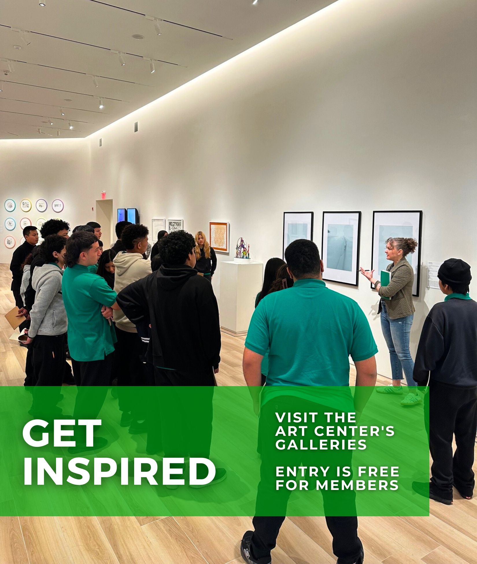 A group of students is gathered in a brightly lit art gallery, attentively listening to a docent who is gesturing toward framed artwork on the wall. The gallery features modern and contemporary art pieces. A green banner overlay at the bottom of the image reads, "GET INSPIRED - Visit the Art Center's Galleries - Entry is Free for Members."