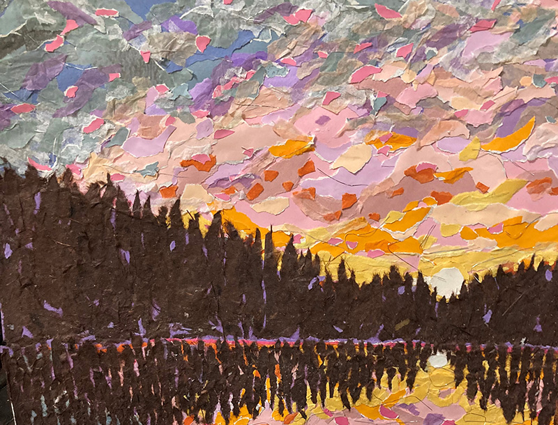 A colorful mixed-media collage depicting a sunset over a lake. Torn pieces of paper in shades of pink, purple, orange, yellow, and gray form a vibrant, textured sky. A dark silhouette of a tree line stretches across the middle of the composition, with its reflection mirrored in the water below. The layered paper technique creates a rich, mosaic-like surface with dynamic color and texture.