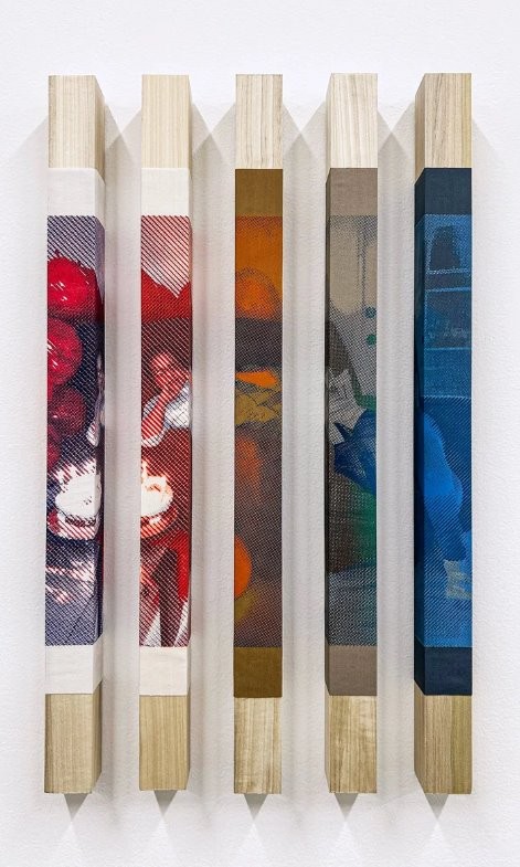 A sculptural/textile artwork — five vertical wooden beams with fabric or printed panels wrapped around their middle sections, showing photographic-looking images in red, orange, and blue tones (titled "Provisional Monument for Aunty Woll").